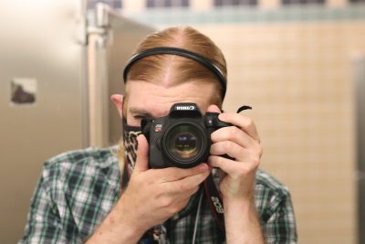 Stephen Slota (the photographer, wearing a green/white/blue plaid collared shirt and black headband) takes a photo in an ITE building bathroom mirror